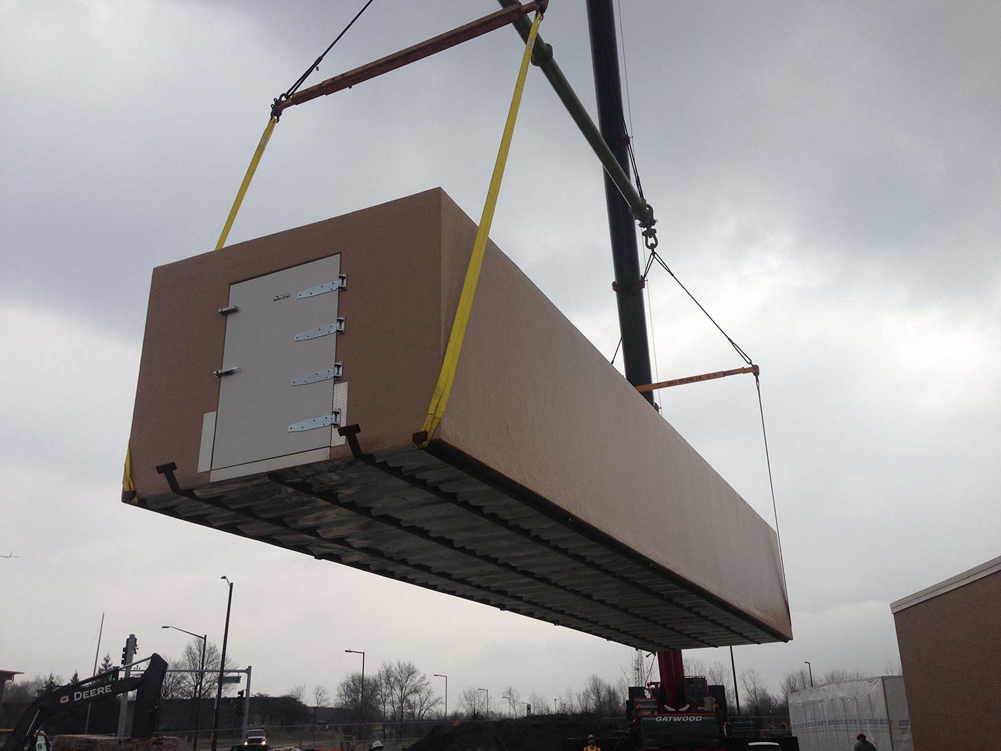 Crane lifting a tan colored walk in freezer for delivery